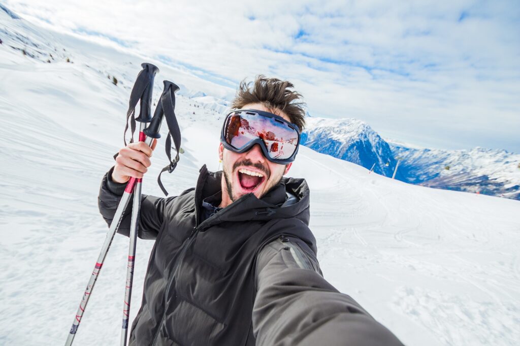 Persona sorridente con occhiali da sci su una montagna innevata.